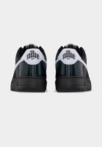 Ζευγάρι μαύρων και λευκών παπουτσιών Nike, φαίνεται από πίσω, δείχνοντας το ανάγλυφο λογότυπο "nike" σε κάθε τακούνι.