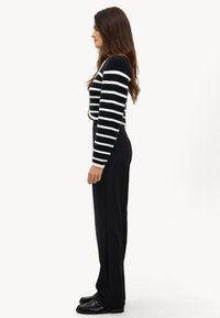 Pull rayé noir et blanc avec un design court, associé à un pantalon noir taille haute et des mocassins noirs, présenté de côté.
