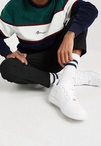 Zapatillas blancas Nike Air Force 1 con puntera perforada, usadas con calcetines blancos con rayas marinas, combinadas con una sudadera con bloques de color.
