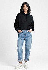 Juodas gobtuvėlis su priekinia kišene, derinamas su šviesiai mėlynomis aukštai juosmeninėmis džinsomis, suvrandomis ant rankogalių, ir baltomis sportbačiais.