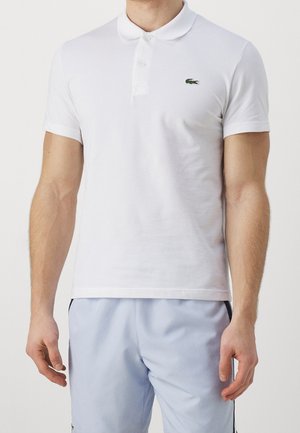 Hvid polo-shirt lavet af bomuld, med en tre-knaps stolpe og et lille grønt broderet krokodillelogo på brystet.