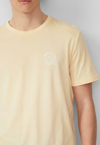 T-shirt en coton jaune clair à manches courtes, avec un col rond et un petit graphique blanc disant "BATTEZ LA CHALEUR" sur la poitrine.