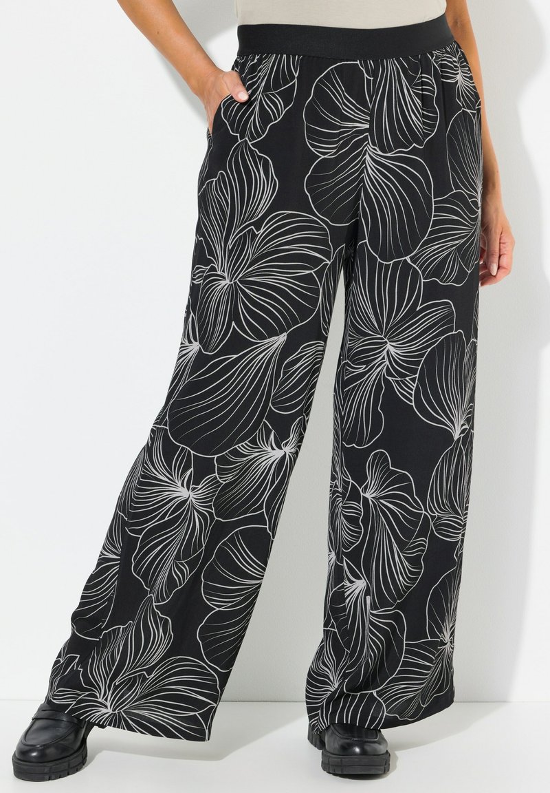 Zwarte wijde broek met een witte bloemenpatroon, voorzien van een elastische tailleband en zijzakken, gemaakt van een lichte stof.