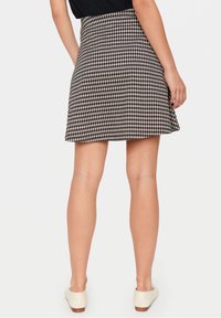 Svart och beige rutig skaterkjol gjord av lättviktsmaterial, med en utsvängd form och midjeband, matchad med vita skor.