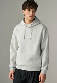 Sudadera gris claro con textura acanalada, capucha ajustable con cordón y corte relajado. Combinada con pantalones negros, que tienen mangas con puños.