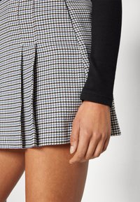 Hame houndstooth mustavalkoinen sinisillä yksityiskohdilla, liehuke suunnittelu ja sileä pinta. Istuva musta pitkähihainen paita on osittain näkyvissä.