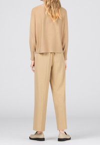 Beżowy miękki sweter z luźnym tyłem, w zestawieniu z luźnymi beżowymi spodniami. Obuwie w jasnym beżu z czarnymi podeszwami.