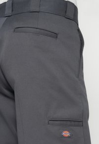 Cargo bukser i mørkegrå stof med en glat tekstur. Har baglomme og et Dickies logo patch på siden. Skræddersyet pasform.