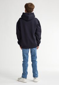 Felpa con cappuccio navy in cotone misto, vestibilità comoda, polsini e orlo a costine, abbinata a jeans in denim blu chiaro e sneakers bianche.