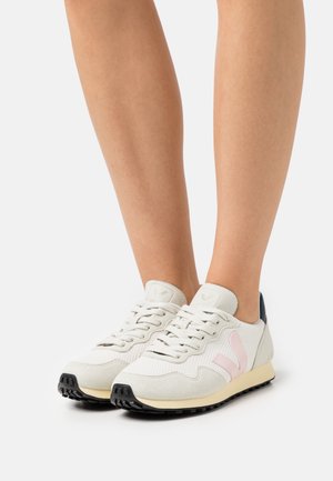 Valkoinen verkko- ja mokkanahan sneakerit, joissa on vaaleanpunaiset yksityiskohdat, musta kumipohja ja nauhakiinnitys; sisältää pyöreän varpaan ja pehmustetun nilkkareunan.