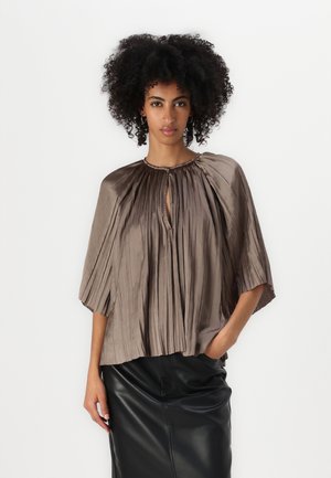 Blusa plissettata color bronzo con maniche corte e larghe e scollatura a chiave, abbinata a una gonna in pelle nera. Dettaglio in tessuto texture visibile.