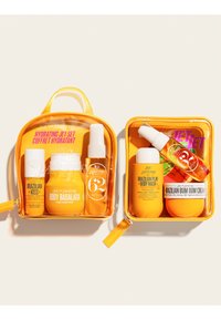 Deux trousses de voyage jaunes contenant des produits de soin Sol de Janeiro, y compris un gommage pour les lèvres Brazilian Kiss, une lotion Body Badalada, un gel douche Brazilian Play et une crème Bum Bum.