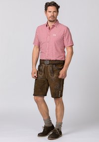 Rutig röd och vit kortärmad skjorta, bruna lädershorts med detaljerad broderi och metalliska accenter, kombinerat med grå knästrumpor och skor.