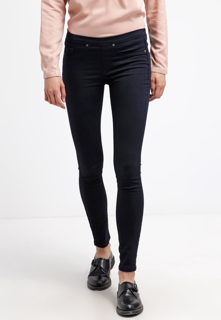 Sotilas siniset skinny farkut, valmistettu sileästä denim-kankaasta, viidellä taskulla ja hienovaraisilla ompeluyksityiskohdilla. Yhdistetty mustiin kenkiin.