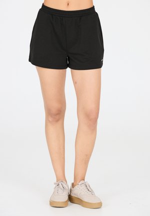 Black athletic shorts with elastic waistband, featuring a relaxed fit and smooth fabric. Paired with beige sneakers and white laces.