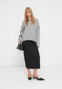 Maglione grigio a coste con spacco laterale, abbinato a una gonna maxi in denim nera. Scarpe slingback nere a punta e una piccola borsa nera.