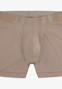Boxers beiges fabriqués en tissu doux, dotés d'une ceinture élastique grise avec "JORDAN" imprimé en évidence. Texture lisse, design anatomique.