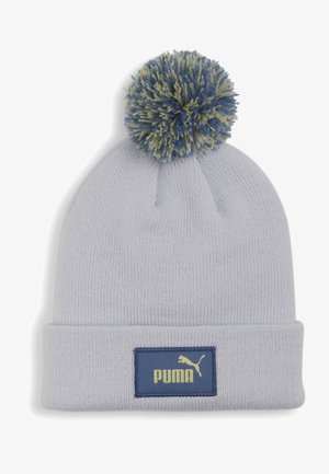 Gorro de punto gris claro con un gran pompón azul y verde en la parte superior. Presenta un parche rectangular azul marino con el logotipo amarillo de "PUMA".