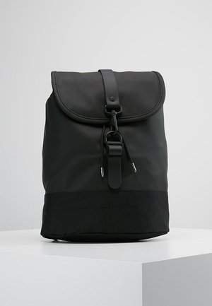 Sac à dos noir avec fermeture à rabat, sangle réglable et cordon sur un socle blanc, sur un fond clair uni.