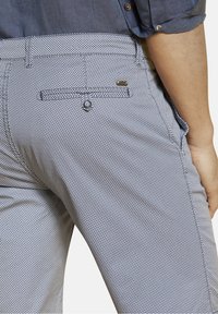 Pantalons bleus à motifs avec une petite texture en losange, dotés d'une poche arrière avec un bouton et d'un accent métallique près de la taille.