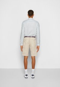 Camicia a maniche lunghe a righe blu chiaro, pantaloni cargo beige, calze bianche e scarpe casual; vista da dietro.