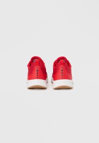 Κόκκινα αθλητικά παπούτσια με υφή στην επάνω επιφάνεια, στρογγυλεμένη φτέρνα, λευκή μεσαία σόλα και καφέ λαστιχένια εξωτερική σόλα. Διαθέτει αντίθετες μαύρες κουκκίδες στη φτέρνα.