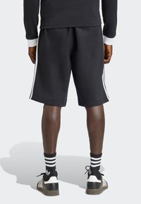 Černé sportovní šortky s bílými pruhy na bocích, vyrobené z měkké, texturované látky. Doplněné černobílými pruhovanými ponožkami a teniskami.