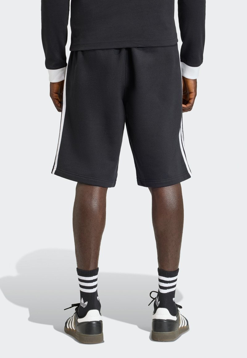 Černé sportovní šortky s bílými pruhy na bocích, vyrobené z měkké, texturované látky. Doplněné černobílými pruhovanými ponožkami a teniskami.