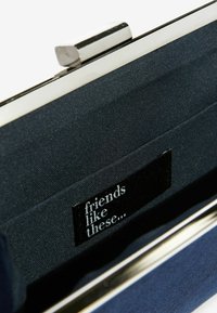 Námořnická textilní kabelka se stříbrným kovovým rámem; vnitřek obsahuje černou etiketu s bílým nápisem "friends like these..." na měkké látkové podšívce.