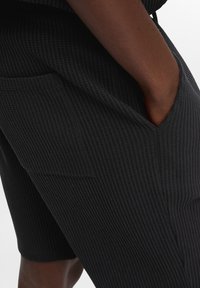 Fekete, texturált rövidnadrág, vájványos mintával, oldalsó zsebekkel és laza szabással. Az anyag puha és könnyűnek tűnik.