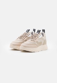 Sneaker sportive beige realizzati in suede e mesh, con una suola spessa, dettagli testurizzati e un'etichetta nera sul tallone.