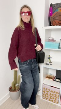 Vinilo bordo turtleneck megztinis, laisvas fasonas; tamsiai džinsai; juoda per petį nešama rankinė; raudoni akiniai nuo saulės. Šalia yra kaktusas vazone. Baltas grindys.