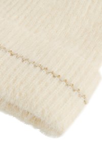 Tela esponjosa de color crema con textura acanalada, que presenta un hilo dorado ondulado a lo largo del borde, mostrando una apariencia suave y acogedora.