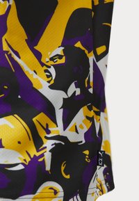 Kortärmad tröja i svart, gult och lila. Har en djärv grafisk design med ansikten och uttrycksfulla poser. Texturerat tyg, med etikett synlig.