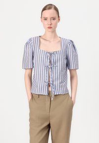 Blouse rayée à manches courtes en bleu et marron avec un col carré et des liens à l'avant, associée à un pantalon tailleur beige clair.