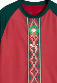 Maillot de sport rouge et vert avec motif géométrique central, emblème de la Fédération Marocaine de Football, et logo Puma blanc sous le blason.