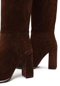 Bruine suede kniehoge haklaarzen met een vierkante hak en een gladde afwerking, met een aansluitende silhoutte en minimale stikdetails.
