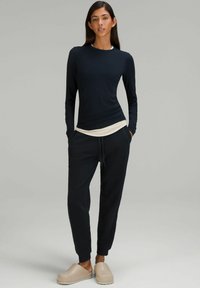 Marineblå langærmet top over en cremefarvet skjorte, parret med mørke joggingsbukser og beige klipklappere. Glat stof, afslappet pasform og elastisk talje.