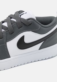 Detailný záber na šedé a biele tenisky s čiernym logom Nike, šedými šnúrkami a polstrovaným golierom na bielom pozadí.