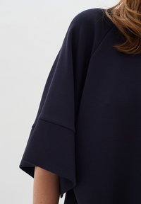 Temno modra oversized majica z širokimi rokavi, izdelana iz mehke tkanine. Ima okroglo ovratnico in sproščen kroj. Gladka tekstura in minimalističen dizajn.