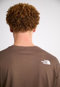 Braunes Baumwoll-T-Shirt mit Rundhalsausschnitt, kurzen Ärmeln und einem weißen Logo auf der oberen Rückseite. Weiche Textur und lockere Passform.