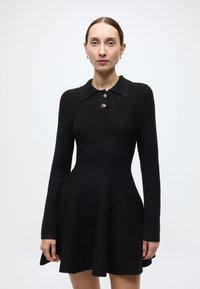 Black wool dress with a fitted bodice, flared skirt, long sleeves, and a collar featuring two gold buttons along the front.