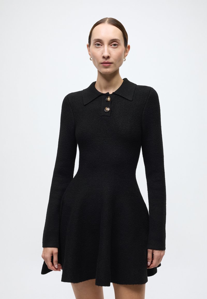 Black wool dress with a fitted bodice, flared skirt, long sleeves, and a collar featuring two gold buttons along the front.