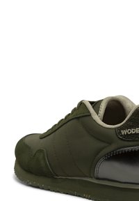 Zapatilla verde oscuro con materiales de ante y sintéticos, forma redondeada, forro interior beige y acento en el talón texturizado negro.