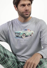 Camisa gris de manga larga con gráfico de un coche clásico, combinada con pantalones de pijama de cuadros verdes y negros con una tela texturizada.