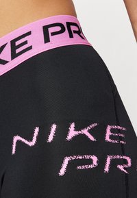 Leggings sportivi neri con un elastico rosa in vita. Presentano il grande testo nero "NIKE" in un design testurizzato lungo il lato.