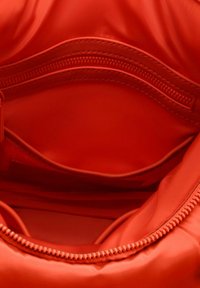 Interno della borsa a tracolla in nylon rosso con texture liscia, dotato di una tasca con zip e scomparti aperti per l'organizzazione.