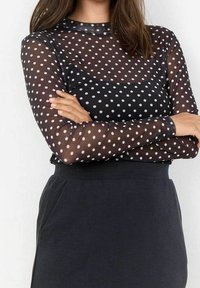 Sort gennemsigtig langærmet bluse med hvide prikker. Blusen har en rund halsudskæring og er kombineret med en mørk, tætsiddende nederdel.