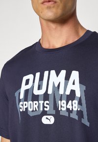 Navy blauwe katoenen t-shirt met opvallende witte tekst 'PUMA SPORTS 1948' en een klein logo aan de onderkant, ronde halslijn en korte mouwen.