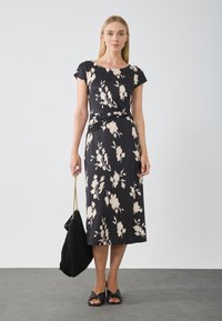 Blommönstrad svart klänning med korta ärmar, knä-lång skärning, mjukt material och draperad midja. Matchas med en svart mockaväska och sandaler.